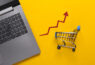 ilustracao-sobre-como-comecar-a-vender-pelo-mercado-livre-com-fundo-laranja-notebook-um-mini-carrinho-de-compras-e-um-seta-vermelha-para-cima