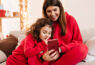 mulher-morena-e-filha-pequena-ambas-usando-pijamas-vermelhos-usam-smartphone-representando-o-dia-das-maes-no-ecommerce