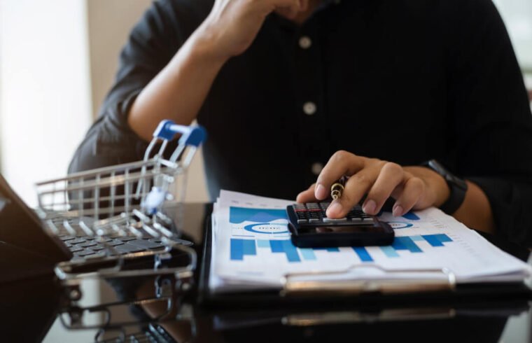 homem-de-blusa-azul-escuro-calcuando-taxa-de-conversao-no-ecommerce-com-graficos-em-papel-e-mini-carrinho-de-compras