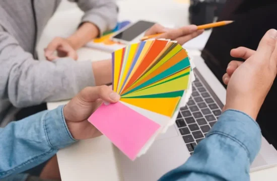 Mãos segurando cores em frente a um computado para escolher a melhor paleta de cores para o seu projeto digital