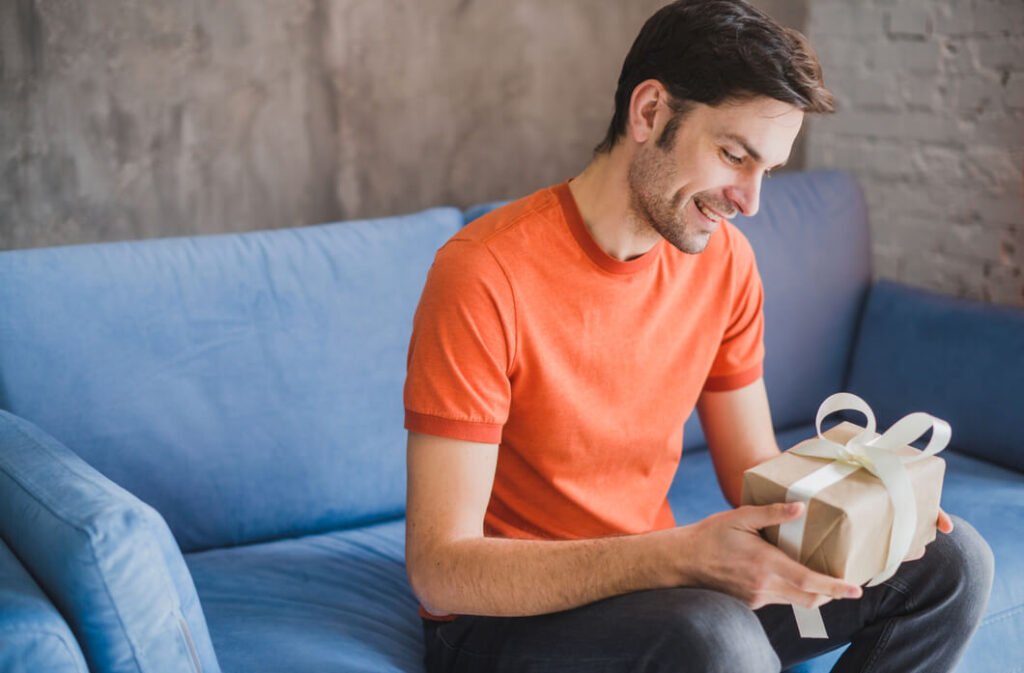 homem-de-camiseta-laranja-em-um-sofa-azul-segura-presente-de-dia-dos-pais-ecommerce